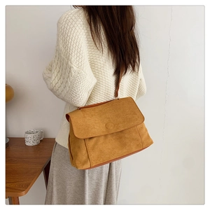 Détail d'un sac bandoulière en velours jaune porté par un mannequin dans un décor sobre