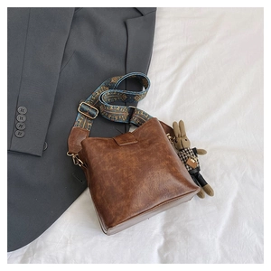 Retro dark brown bucket bag with ethnic blue strap and rabbit charm on grey blazer