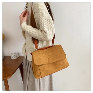 Détail d'un sac bandoulière en daim jaune gingembre avec une large sangle sur un pull blanc
