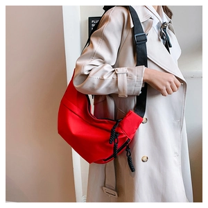 Detail of red crossbody bag featuring black adjustable strap and woven zipper pull tabs