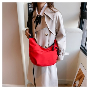 Detail of red nylon crescent bag with adjustable black strap on a beige trench coat