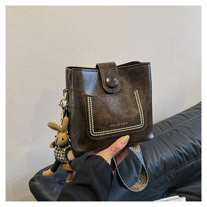 Detail of dark brown leather bucket bag with rivet pocket and colorful embroidered strap