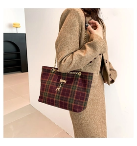 Detail of red and green plaid chain bag with golden deer charm and metallic clasp