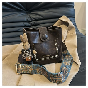 Detail of vintage dark brown bucket bag with patterned strap and cute rabbit pendant