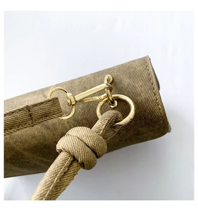 Detail of golden metal hook attachment on textured fabric crossbody bag with knot strap