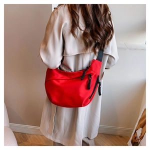 Detail view of red crescent bag with textured fabric and black woven cord zipper pulls