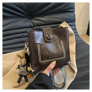 Detail of retro dark brown bucket bag with wide jacquard strap and plush bunny charm