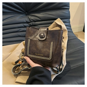 Close-up of vintage brown leather bucket bag with embroidered strap and bear charm