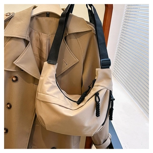Detail of beige nylon crescent bag featuring black adjustable strap and woven zipper pull