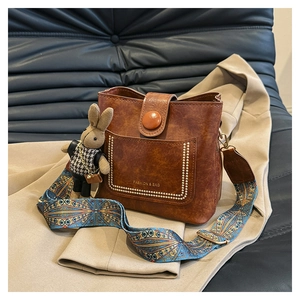 Detail of vintage brown bucket bag featuring gold stud accents and a cute bunny pendant