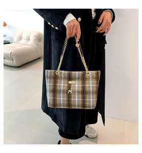 Close-up of tartan wool tote bag with golden chain handle and deer metal pendant