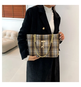 Detail of wool plaid tote bag with gold chain strap and deer charm on a winter coat