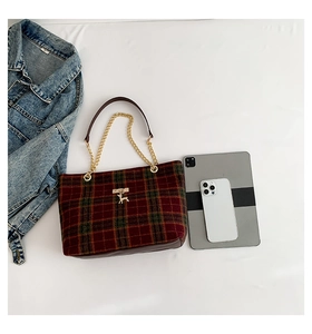 Detail of red and green plaid tote bag with golden chain strap and deer metal logo