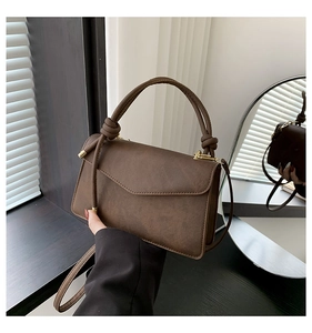 Detailed view of deep brown flap square bag with decorative knotted top handle