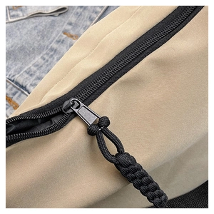 Detail of khaki nylon bag with black zipper and paracord puller on denim background