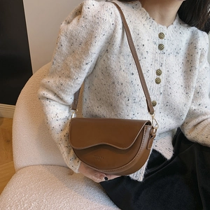 Sacoche classique en cuir mat marron foncé portée en bandoulière sur un cardigan blanc