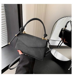 Detail of a matte black mini crossbody bag with a knotted handle and gold metal rings