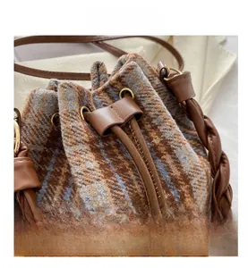 Close-up of checkered drawstring bucket bag featuring a woven handle and leather trim