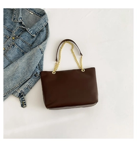 Flat lay of a dark brown leather tote bag with gold chain strap next to denim jacket