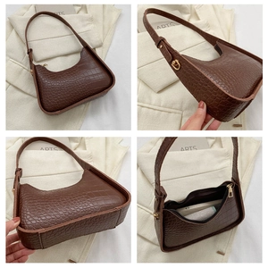 Detail view of dark brown crocodile-embossed underarm bag with gold metal zipper