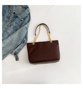 Detail of a dark brown leather tote bag with gold chain straps and a denim jacket
