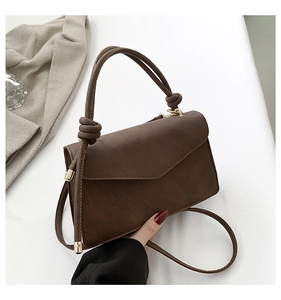 Detail of dark brown matte handbag featuring a cylindrical knot handle and gold hardware