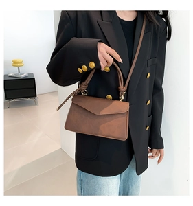 Close-up of brown vintage leather crossbody bag featuring unique knotted handle and gold metal