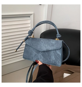 Detailed shot of a blue denim handbag with knot handle and elegant gold hardware details