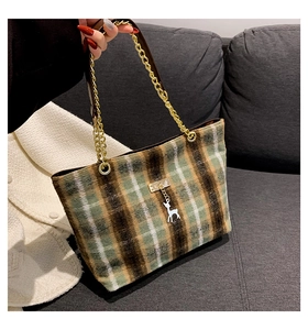 Detailed macro view of green plaid wool tote bag with gold chain and silver deer pendant
