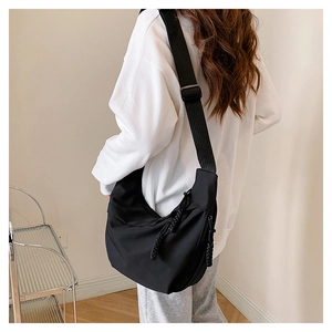 Detail of adjustable wide shoulder strap and woven rope zipper on a black nylon crossbody bag