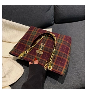 Detail of red plaid tote bag featuring golden deer emblem and leather chain strap