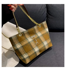 Detail of checkered tote bag with golden chain strap and deer pendant on wool fabric