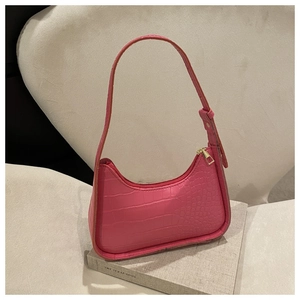 Borsa baguette rosa coccodrillo con cerniera dorata appoggiata su libro di lino