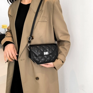 Detail of a black quilted crossbody bag with a silver twist lock on a beige trench coat