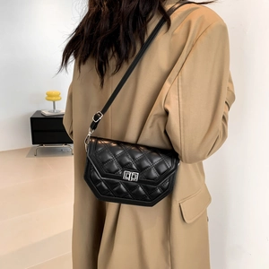 Close-up of black quilted crossbody bag with silver twist lock on a beige blazer
