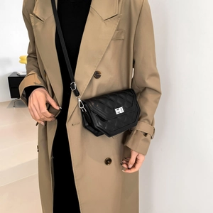 Close-up of black quilted crossbody bag with silver rotating lock on a beige coat