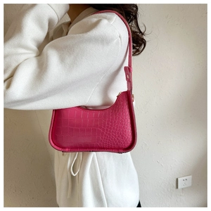 Hot pink crocodile embossed crescent bag worn by a model in a minimalist setting