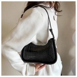 Dettaglio della borsa baguette nera coccodrillo indossata da una modella in giacca tweed