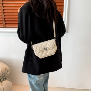 Detail of cream quilted crossbody bag with silver twist lock on a minimalist model shot