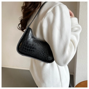 Detail of black faux crocodile texture on a retro shoulder bag worn by a model