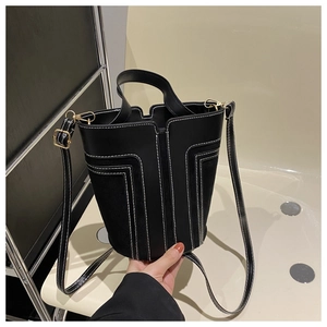 Dettaglio borsa a secchiello nera con cuciture bianche, texture miste e metallo oro