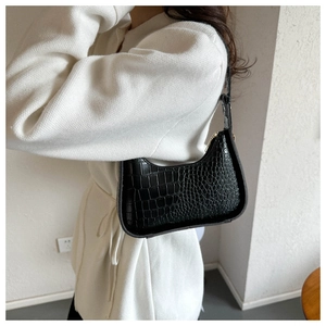 Modella che indossa una borsa sottobraccio nera a motivo coccodrillo con maglia bianca
