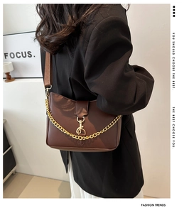 Detail of a dark brown shoulder bag with a gold musical note clasp and thick chain strap