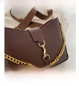 Close-up of dark brown leather bag with chunky gold chain and wide fabric strap