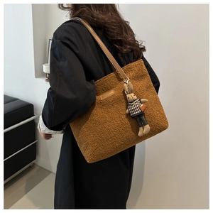 Detail of brown plush tote bag with leather strap and cute rabbit charm on a model