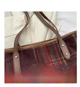 Close-up of vintage plaid tote bag texture with brown leather strap and metal logo