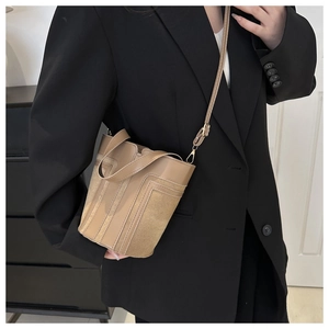 Dettaglio della borsa a secchiello kaki con decoro in pelle a T e tessuto materico