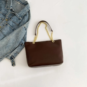 Brown faux leather tote bag with chain strap and denim jacket on white fabric background