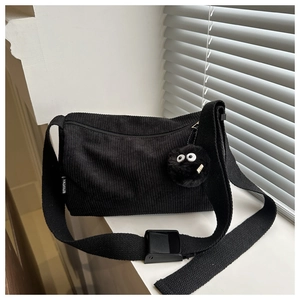 Close-up of black corduroy tote bag featuring wide strap and fuzzy charm with eyes