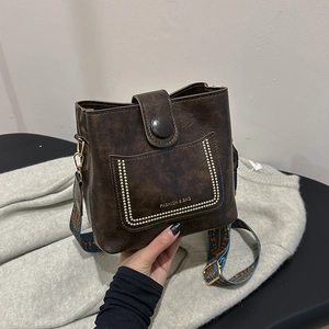 Retro brown bucket bag with wide ethnic strap and gold studs shown in hand